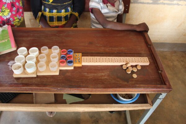 Posées sur une table en bois de gauche à droite, une première planche avec six gros godets en plastique. Une seconde avec six godets plus petits, une troisième avec six godets de taille encore plus petite avec six vis. Enfin, une réglette en bois apportée de Suisse.